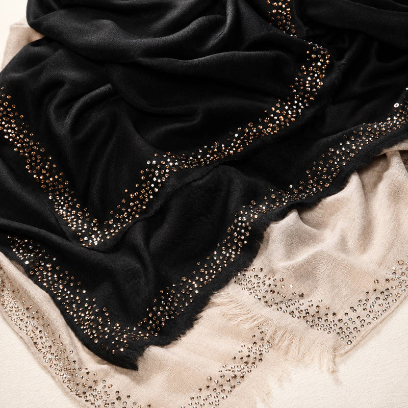 Black cashmere scarf with crystals by Swarovski on top of another natural cashmere scarf with cystals by Swarovski on a white background